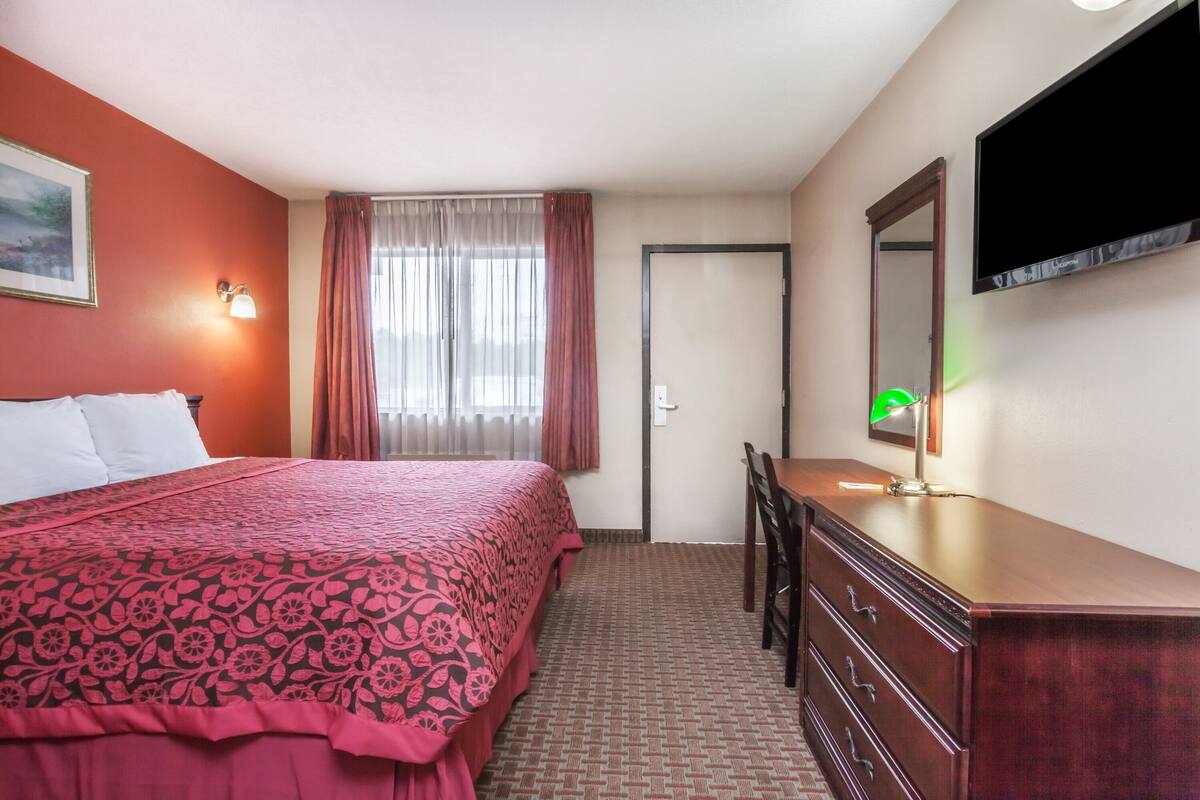 A hotel room with a bed, a dresser, a desk, a chair, a television, and a window with curtains.