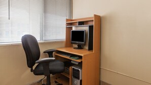 A computer desk with a monitor, keyboard, and chair in a room with beige walls and a window with blinds. - Red Carpet Inn (Elkton)