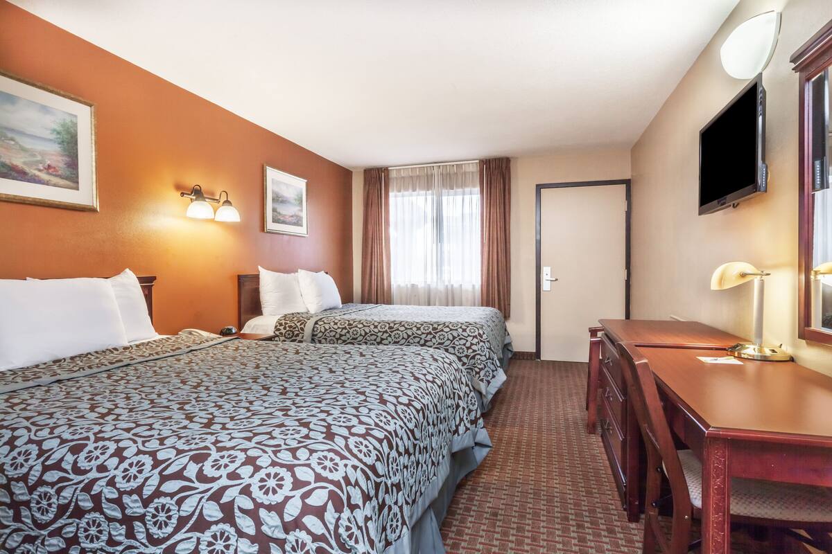 A hotel room with two beds, a desk, a chair, a TV, and a window with curtains.