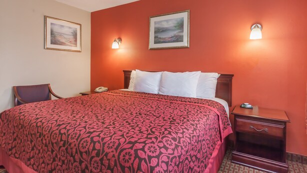 A hotel room with a large bed, two bedside tables, a chair, and two wall-mounted lamps. - Red Carpet Inn (Elkton)