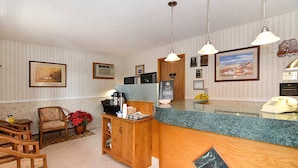 A reception area with a wooden desk, a chair, a potted plant, framed pictures on the wall, and a telephone.