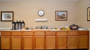 A kitchen with wooden cabinets, a clock, and framed pictures on the wall.