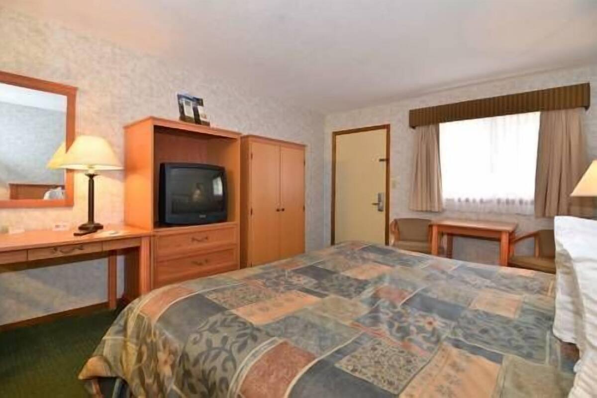 A hotel room with a bed, a desk with a lamp, a television, and a door.