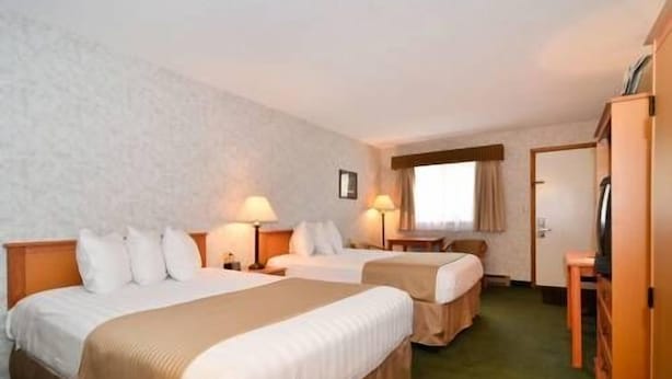A hotel room with two beds, a desk, a chair, a TV, and a window with curtains.