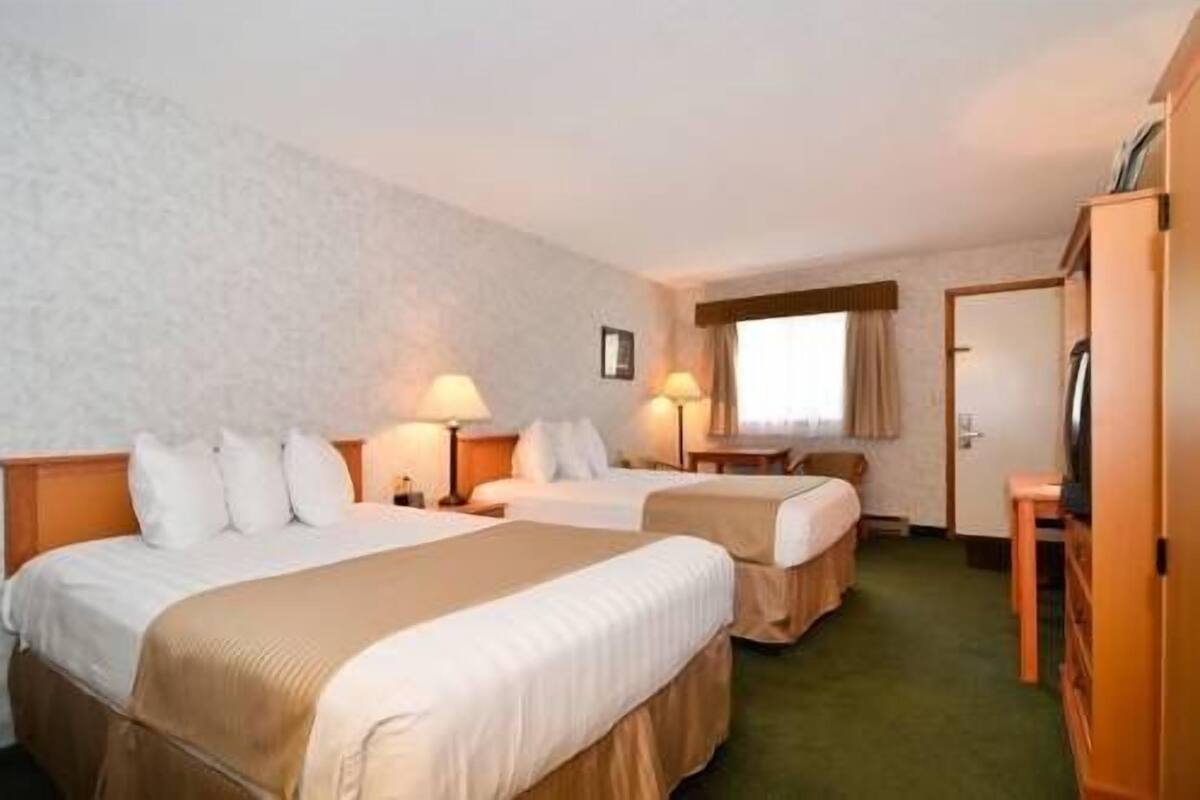 A hotel room with two beds, a desk, a chair, a TV, and a window with curtains.