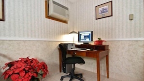 A small office with a desk, computer, and chair. There is a potted plant and a framed picture on the wall.