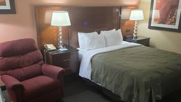 Une chambre d’hôtel avec un lit, deux lampes de chevet, un fauteuil rouge, un téléphone et un tableau encadré au mur.