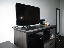 Un televisor de pantalla plana sobre un mueble de madera, con un control remoto, un parlante pequeño y una caja de pañuelos.