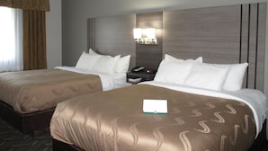 A hotel room with two beds, a nightstand, and a wall-mounted lamp. - Quality Inn Kirksville (Kirksville)