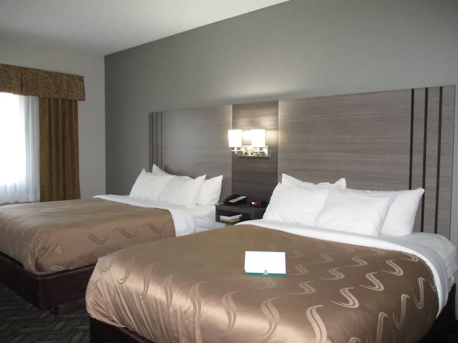 Een hotelkamer met twee bedden, een nachtkastje en een lamp aan de muur.