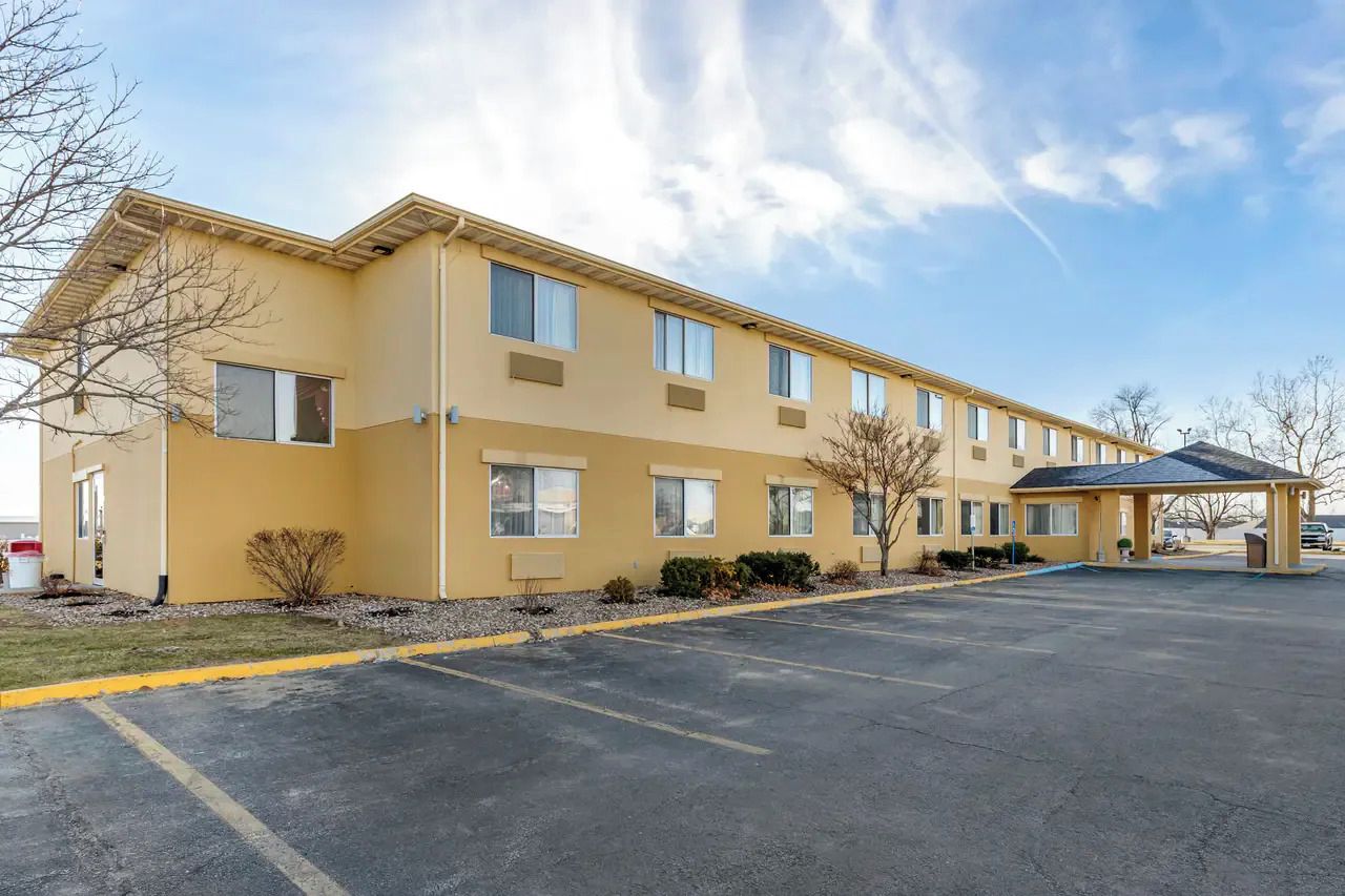 A multi-story hotel with a flat roof, a covered parking area, and a clear sky.