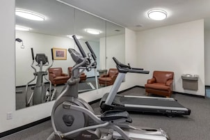 Un gimnasio con equipo de cardio, una cinta de correr y dos sillones de cuero marrón.