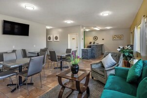 A modern living room with a dining area, a flat-screen TV mounted on the wall, and a reception desk in the background.