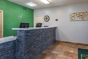 A reception desk with a green wall, a clock, and a decorative wall piece. - Quality Inn Kirksville (Kirksville)