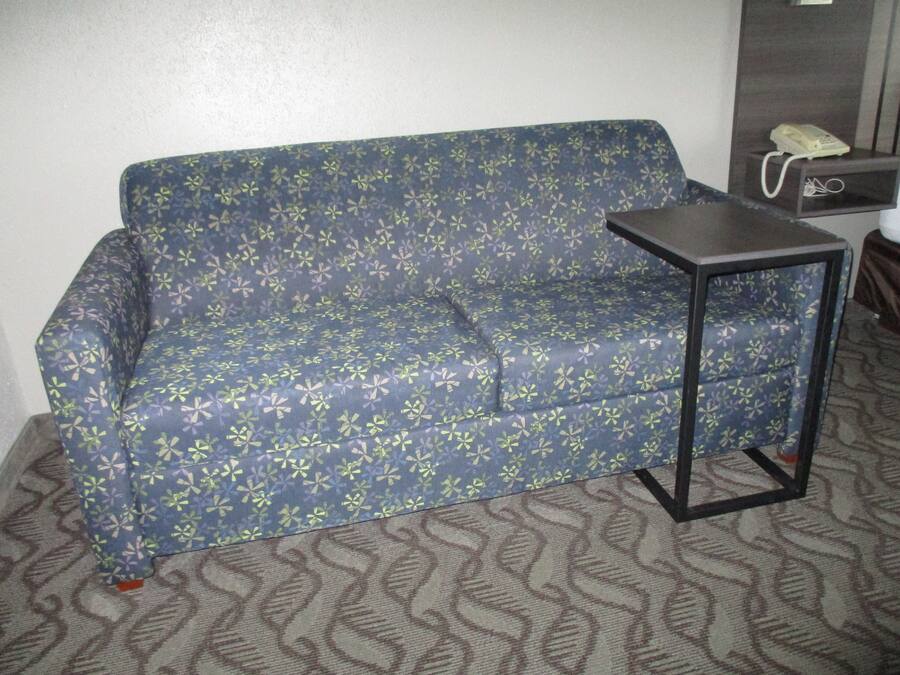 Un sofá azul con estampado floral, una mesita auxiliar negra pequeña y un teléfono sobre un estante de madera.
