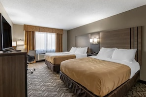 A hotel room with two beds, a desk, a chair, a desk lamp, a TV, and a window with curtains. - Quality Inn Kirksville (Kirksville)