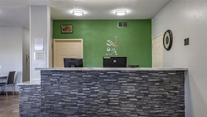 A reception desk with a stone-textured counter, a green wall with the hotel logo, a clock, and a door. - Quality Inn Kirksville (Kirksville)
