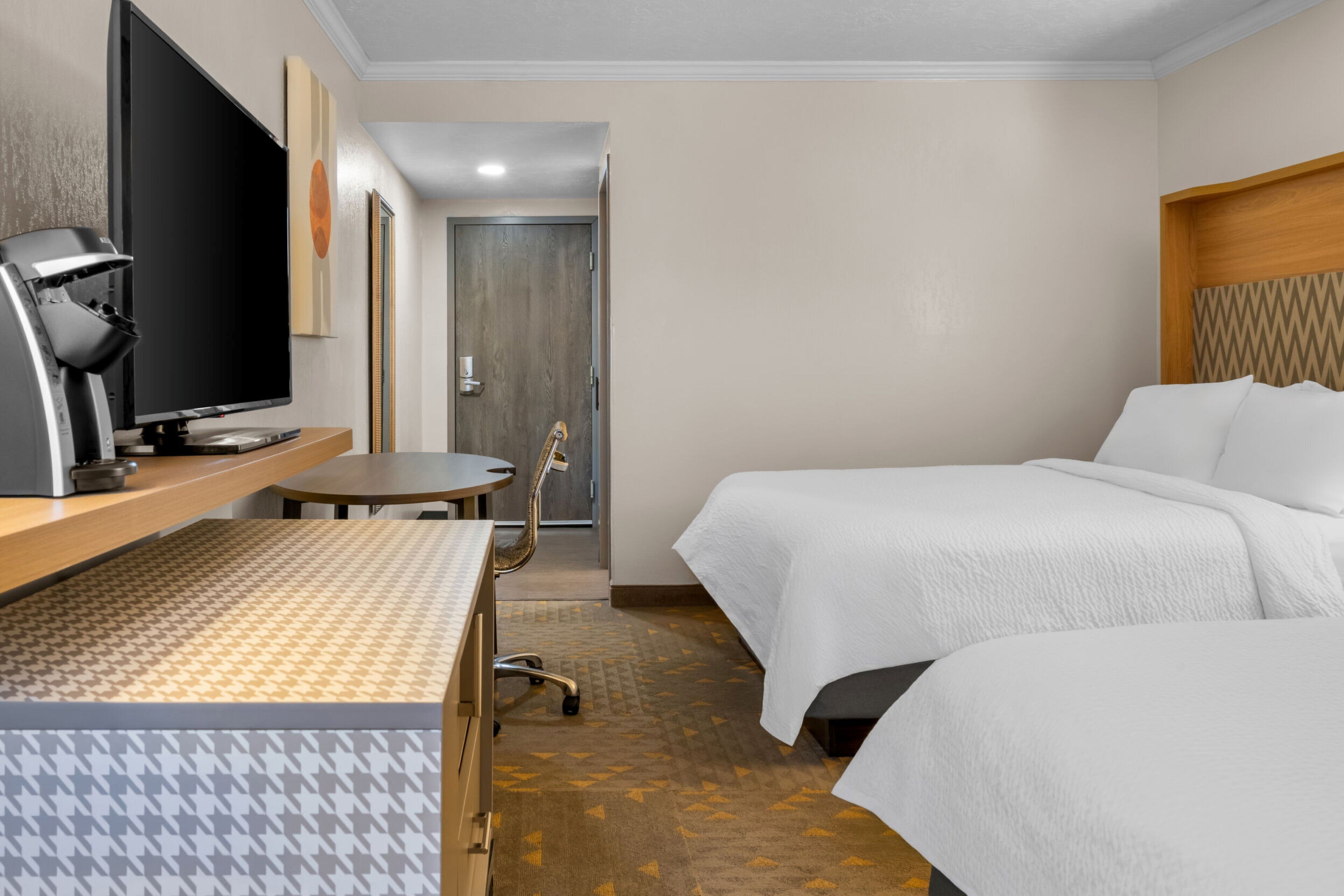 A hotel room with two beds, a desk with a computer, a television, and a door leading to another room.