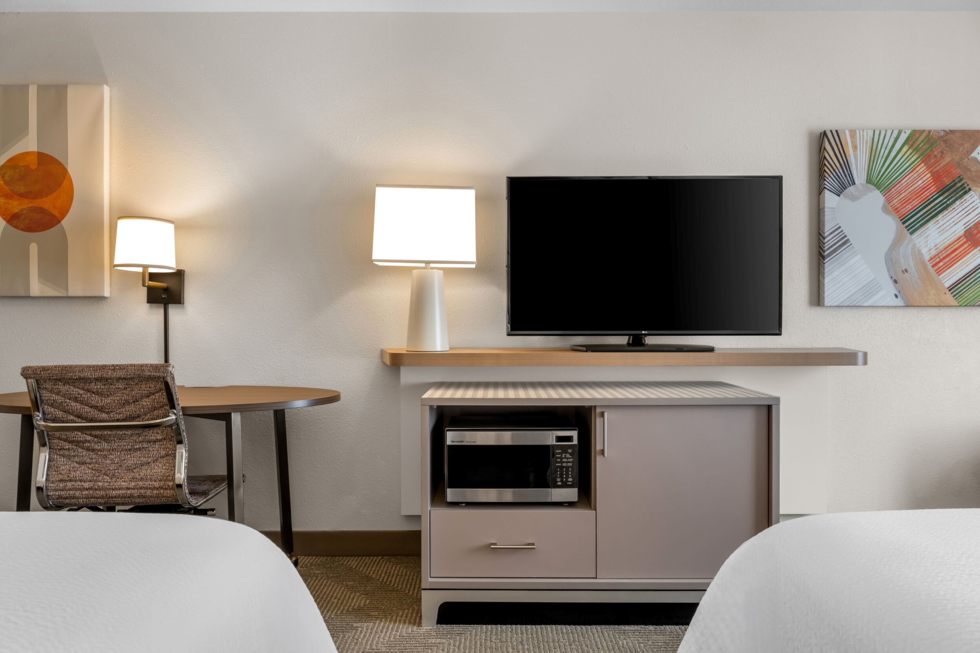 Une chambre d’hôtel comprenant un lit, un bureau avec une lampe, une télévision, un four à micro-ondes et un placard.