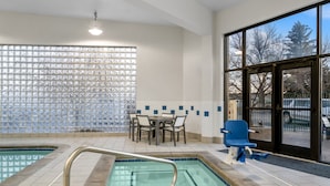 An indoor swimming pool with a glass wall, a table with chairs, and a blue chair. - Holiday Inn Rock Springs by IHG (Rock Springs)