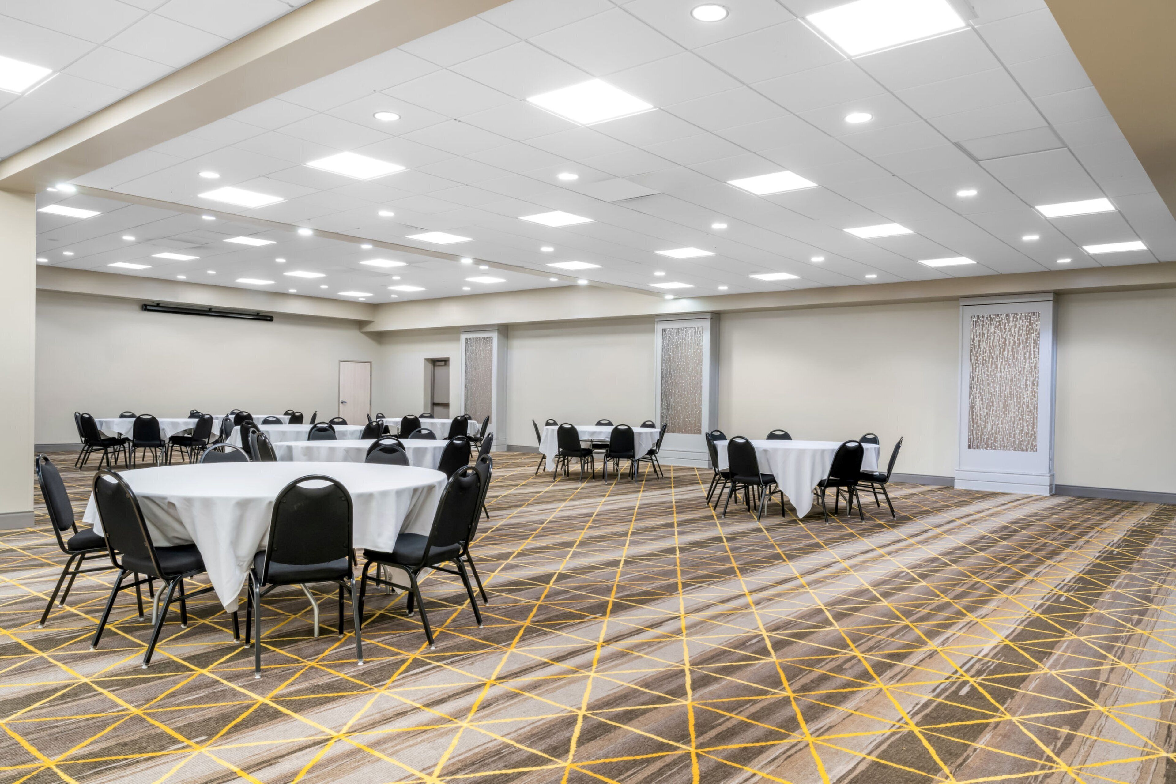 A conference room with round tables and chairs, carpeted floor, and ceiling lights.