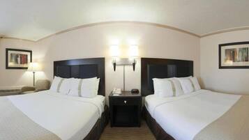 A hotel room with two beds, a nightstand between them, and a wall-mounted lamp.