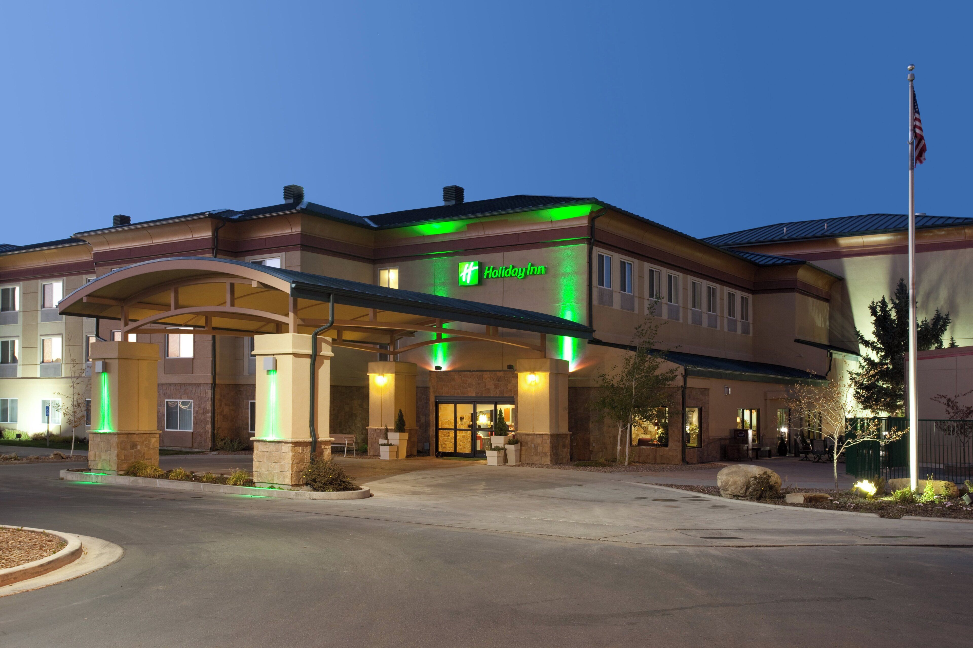 A Holiday Inn hotel with a covered entrance, outdoor seating, and a flagpole.