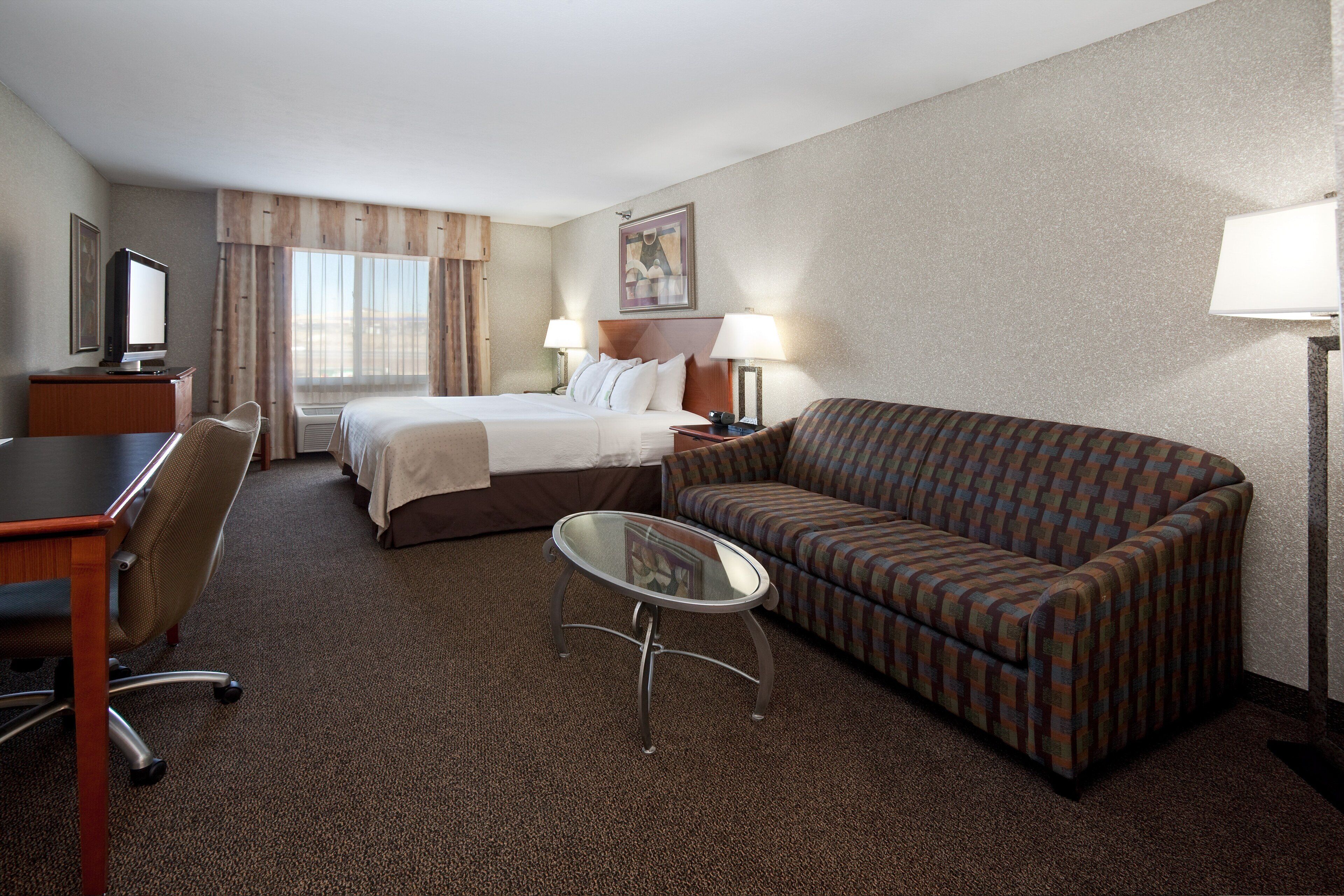 A hotel room with a bed, a sofa, a desk, a chair, and a small table.