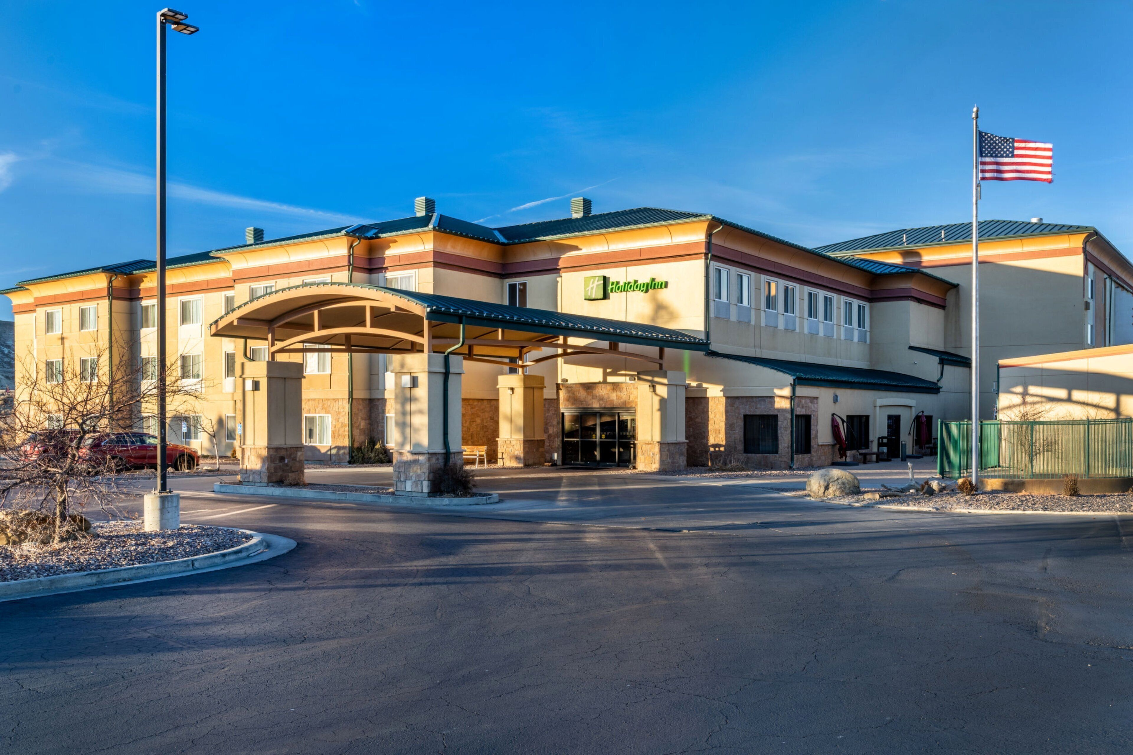A Holiday Inn Express hotel with a covered entrance, a flagpole with an American flag, and a clear sky.