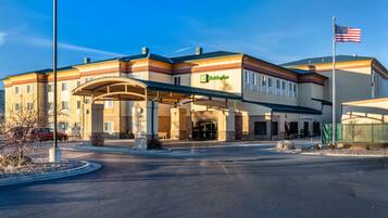 A Holiday Inn Express hotel with a covered entrance, a flagpole with an American flag, and a clear sky.