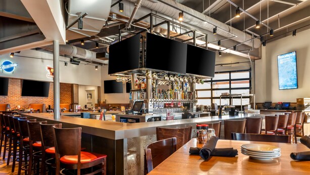 Eine moderne Bar mit einer langen Theke, mehreren Barhocker und einer Auswahl an Flaschen.