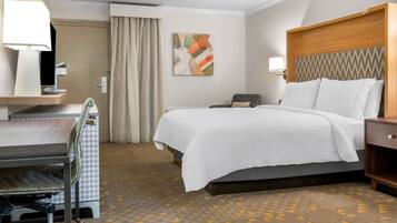 A hotel room with a bed, desk, chair, and a painting on the wall.