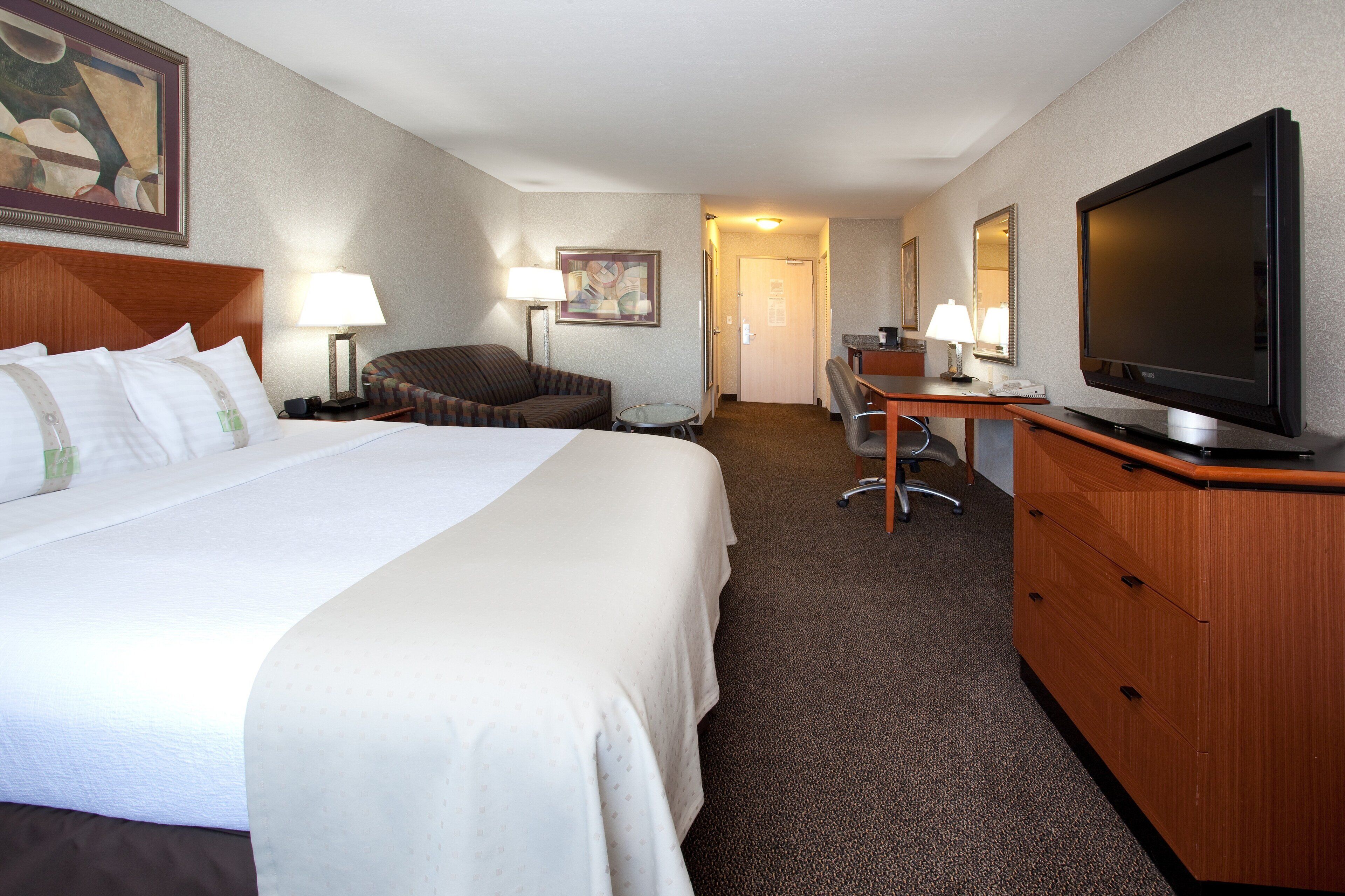 A hotel room with a large bed, a desk, a chair, a television, and a lamp.