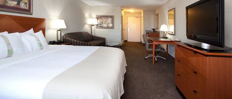 A hotel room with a large bed, a desk, a chair, a television, and a lamp.