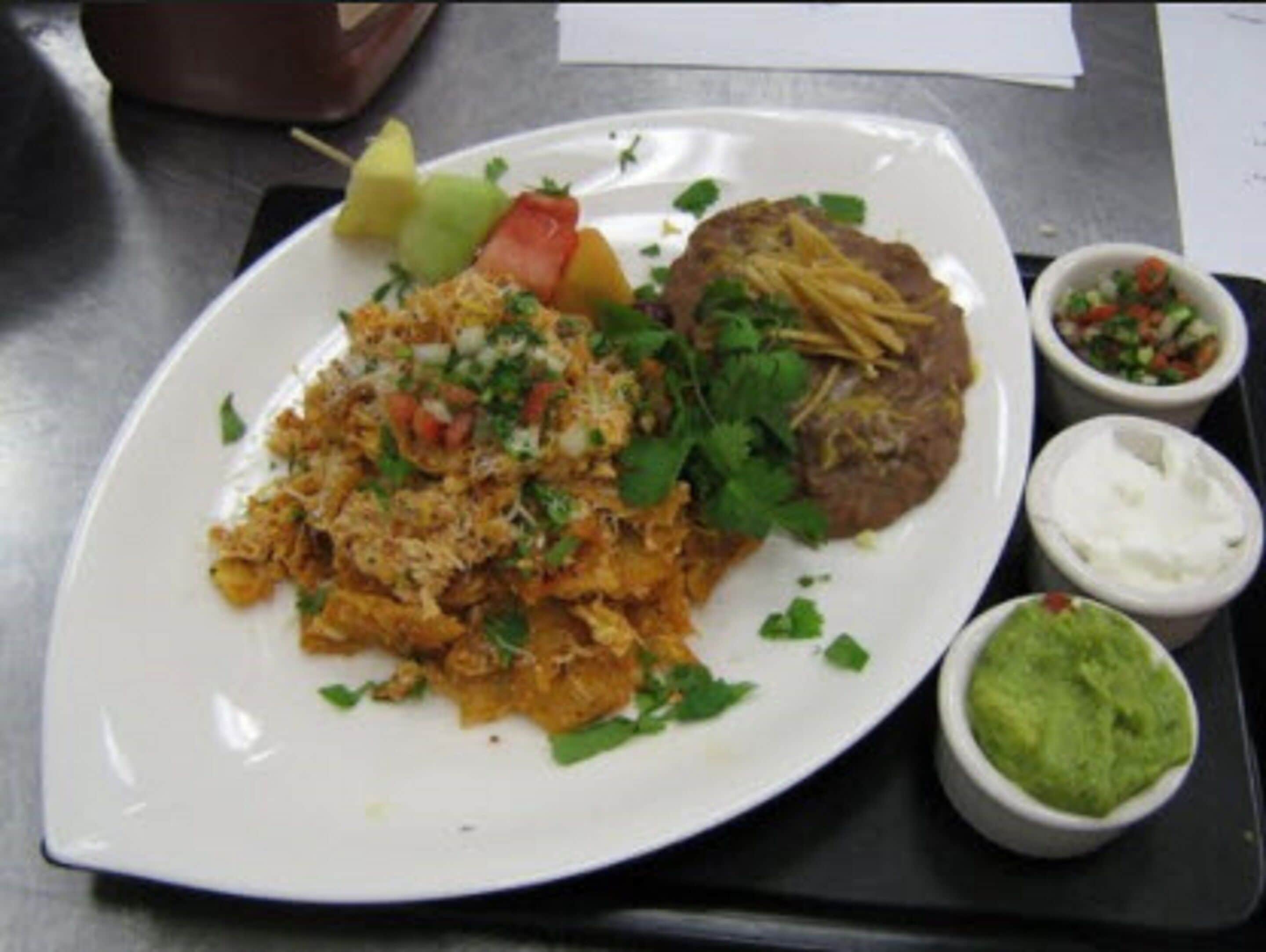 A plate of food with rice, beans, and vegetables, accompanied by small bowls of guacamole and salsa.