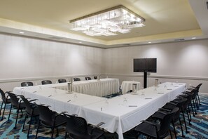 Uma sala de conferência com uma mesa comprida, cadeiras, uma tela de projetor e um candelabro.