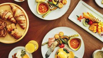Un desayuno con varios platos de comida, incluyendo cruasanes, huevos y fruta.