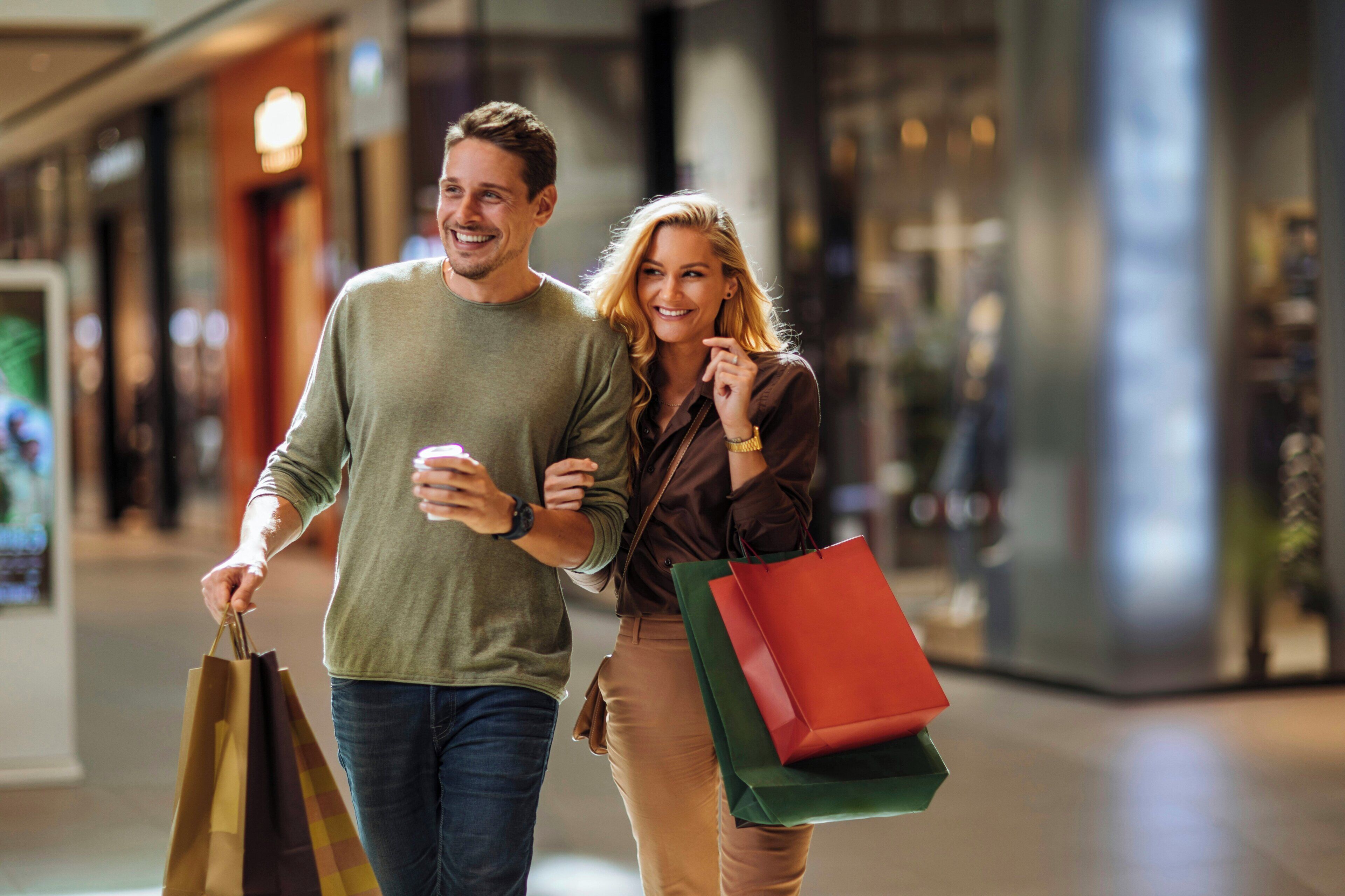 Una pareja camina por un centro comercial llevando bolsas de compras.