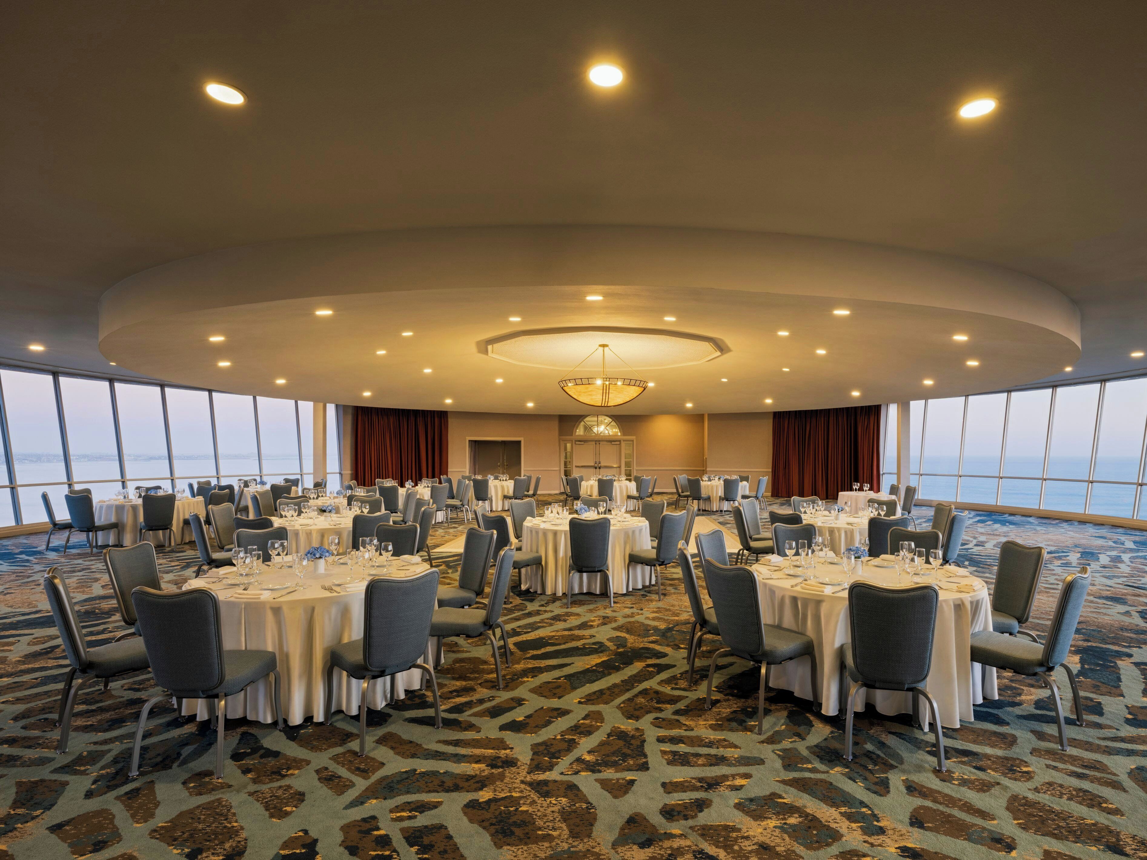 Un gran salón de banquetes con mesas redondas, sillas y una lámpara central.