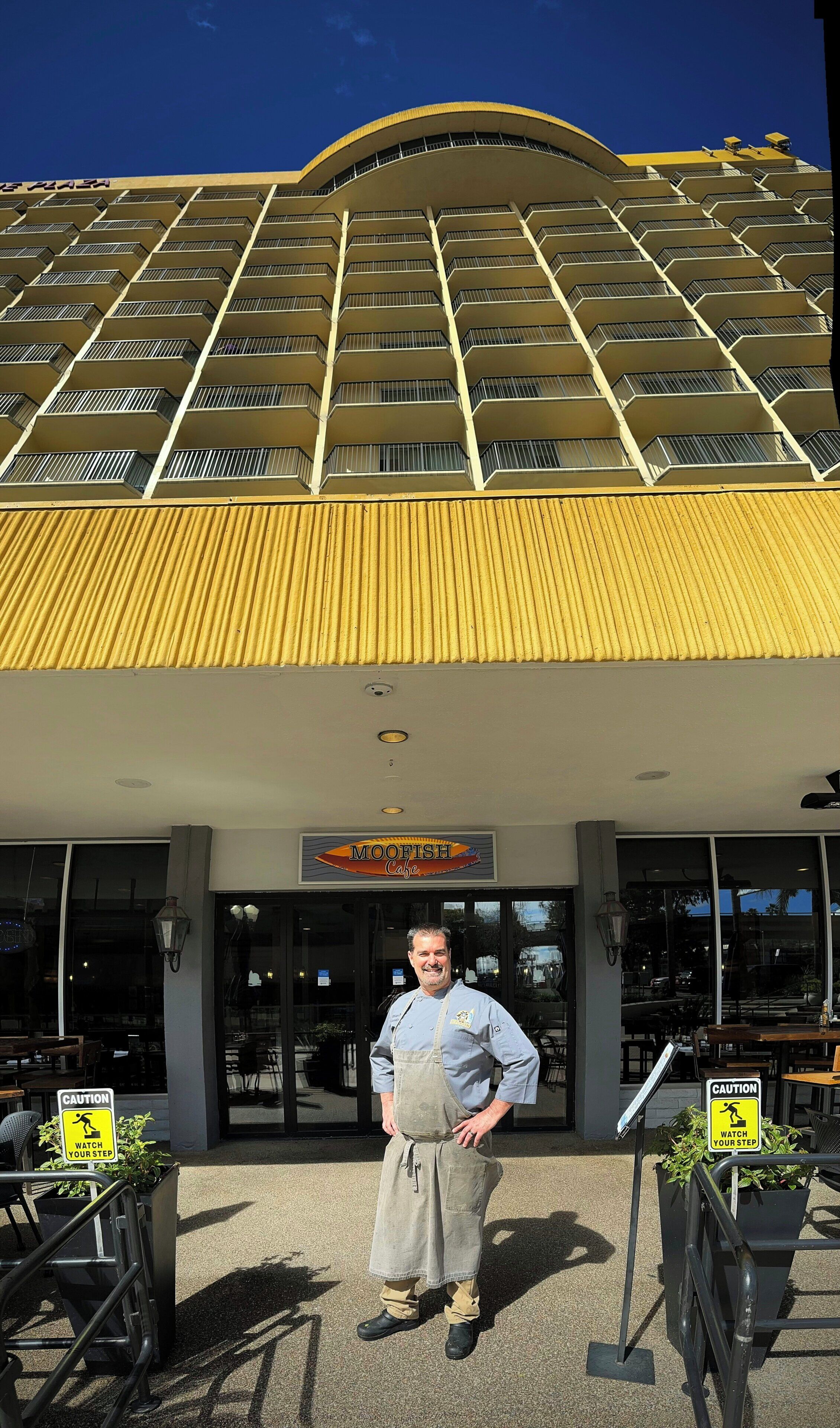 A man standing in front of a building with a curved yellow roof and a sign that reads 'MOOFISH Cafe'.