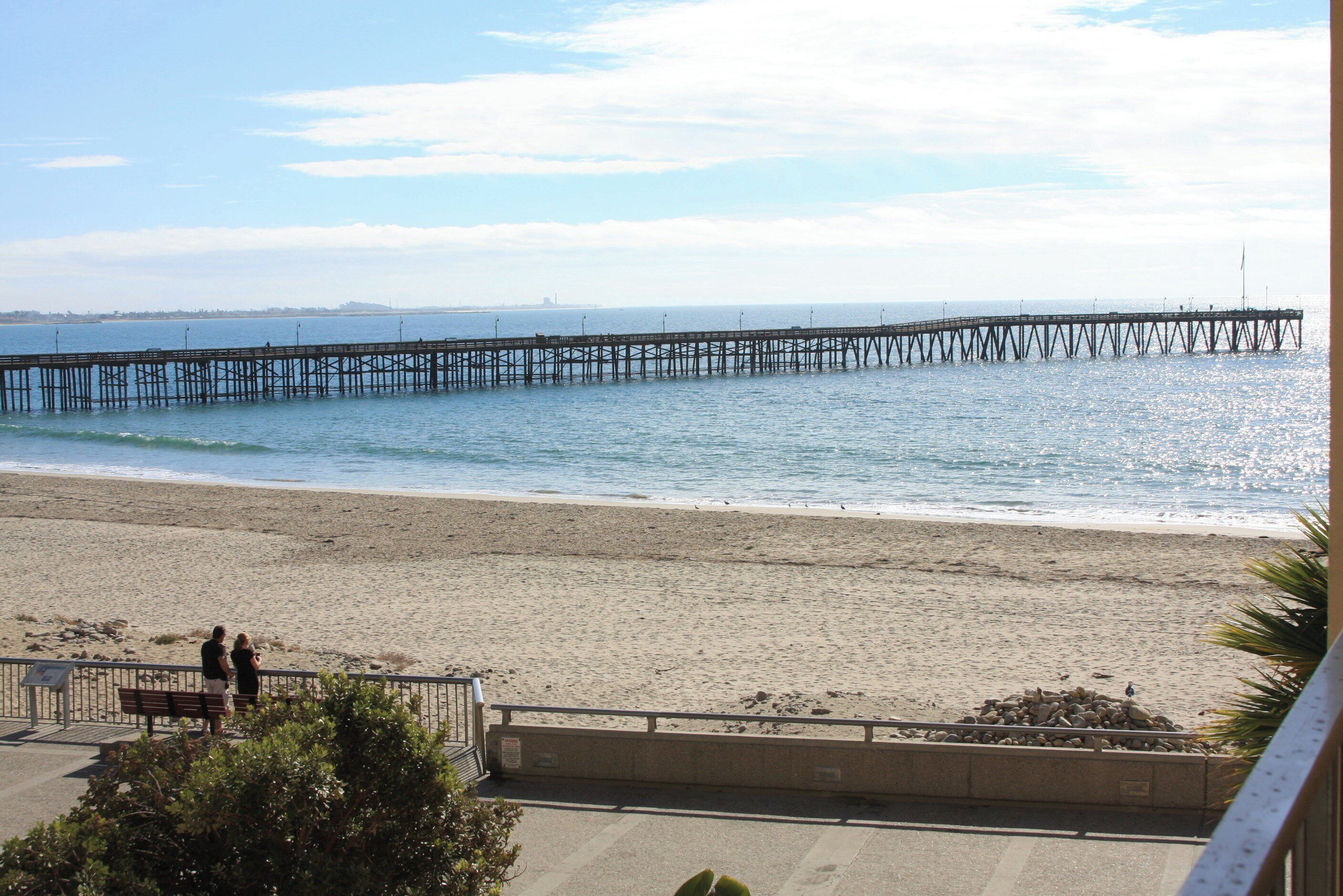 A beach with a pier extending into the water, a sandy shore, and a few people walking along the beach.