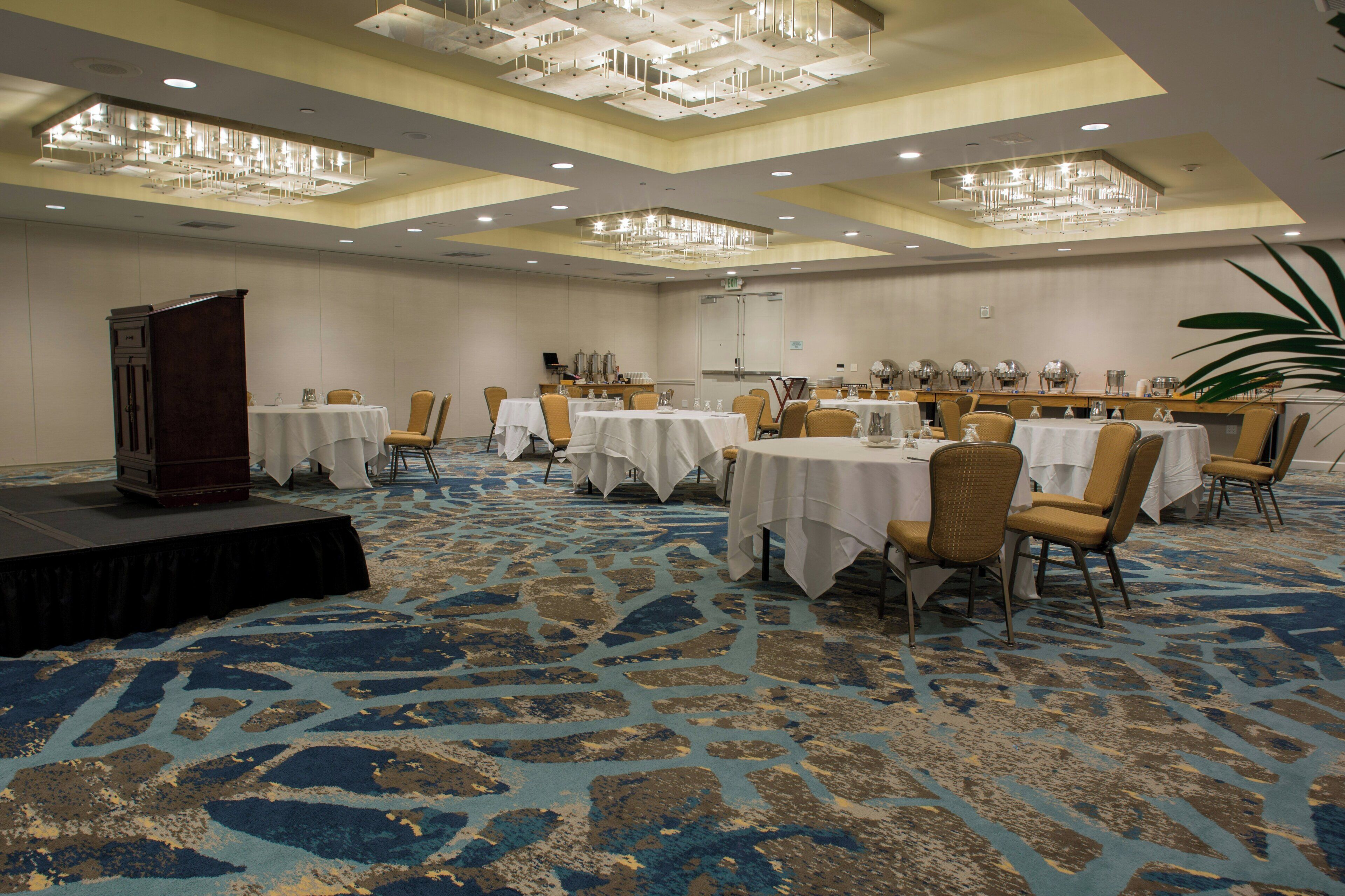 A banquet hall with multiple round tables, chairs, and a stage.