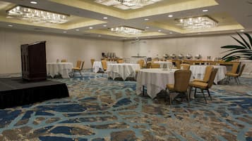 A banquet hall with multiple round tables, chairs, and a stage.