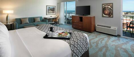 A hotel room with a bed, a desk, a television, and a balcony with a view.