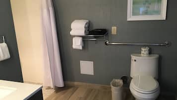A bathroom with a toilet, a trash can, a towel rack with towels, a shower curtain, and a framed inspirational quote on the wall.