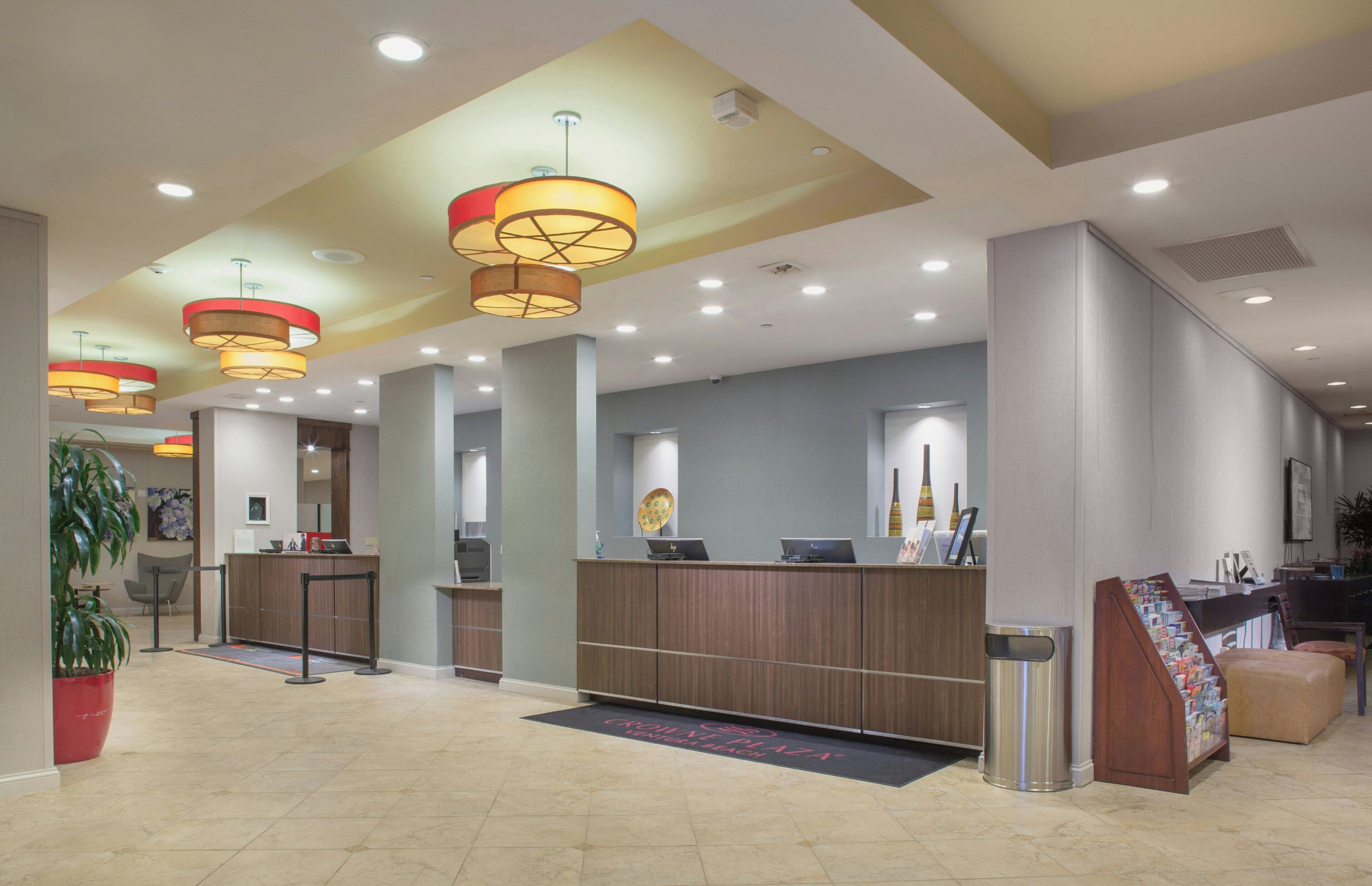 A hotel lobby with a reception desk, multiple computer stations, and a large plant.