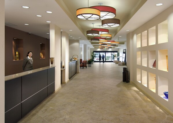 A hotel reception area with a reception desk, a waiting area with chairs, and a hallway with a tiled floor. - Crowne Plaza Ventura Beach by IHG (Ventura)