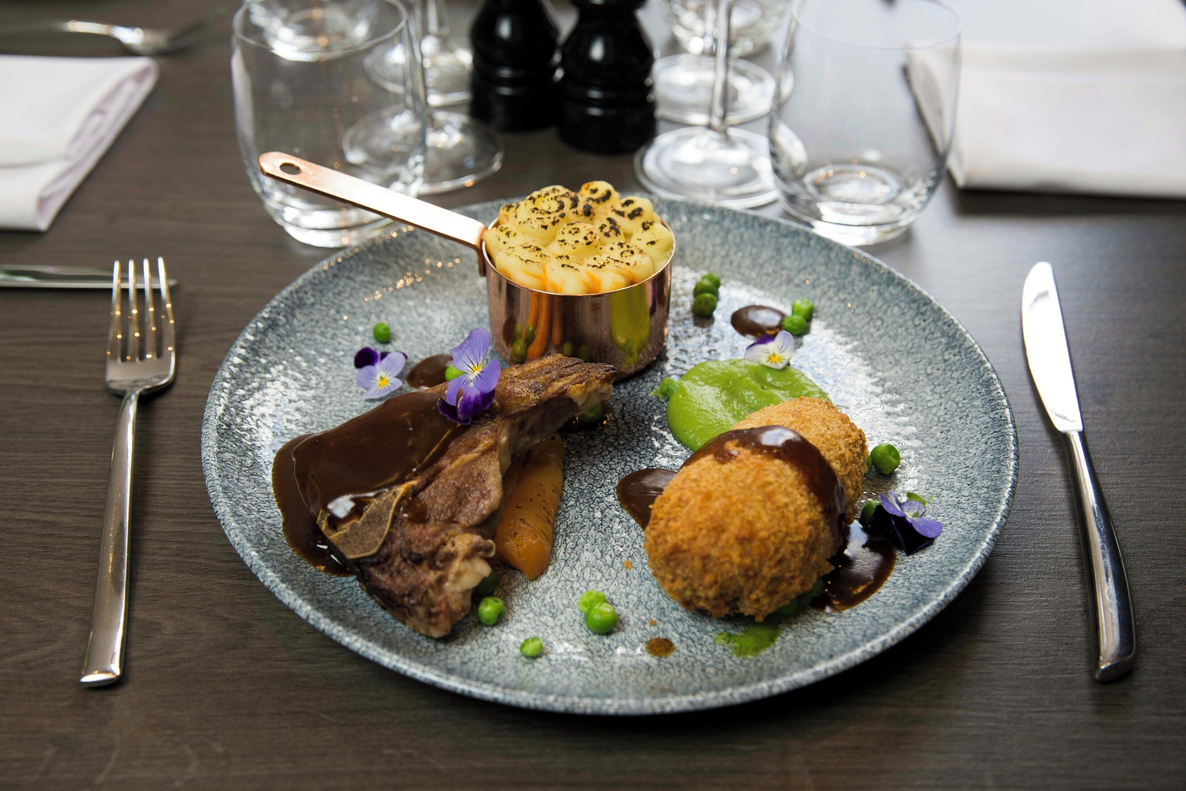 A plate of food with a variety of items including a meat dish, a potato dish, and some greens.