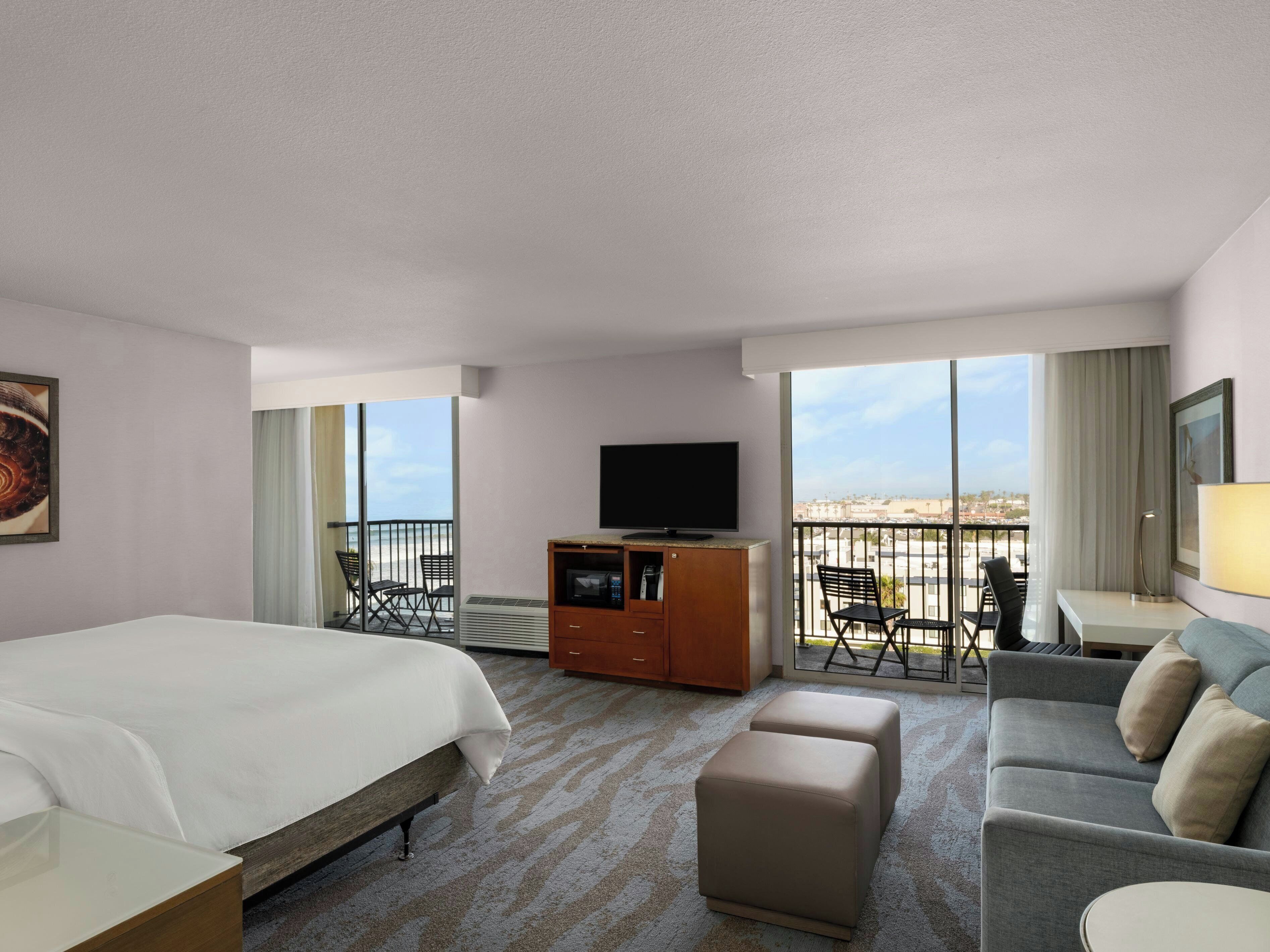 A hotel room with a bed, a sofa, a TV, a desk, and a balcony with a view.