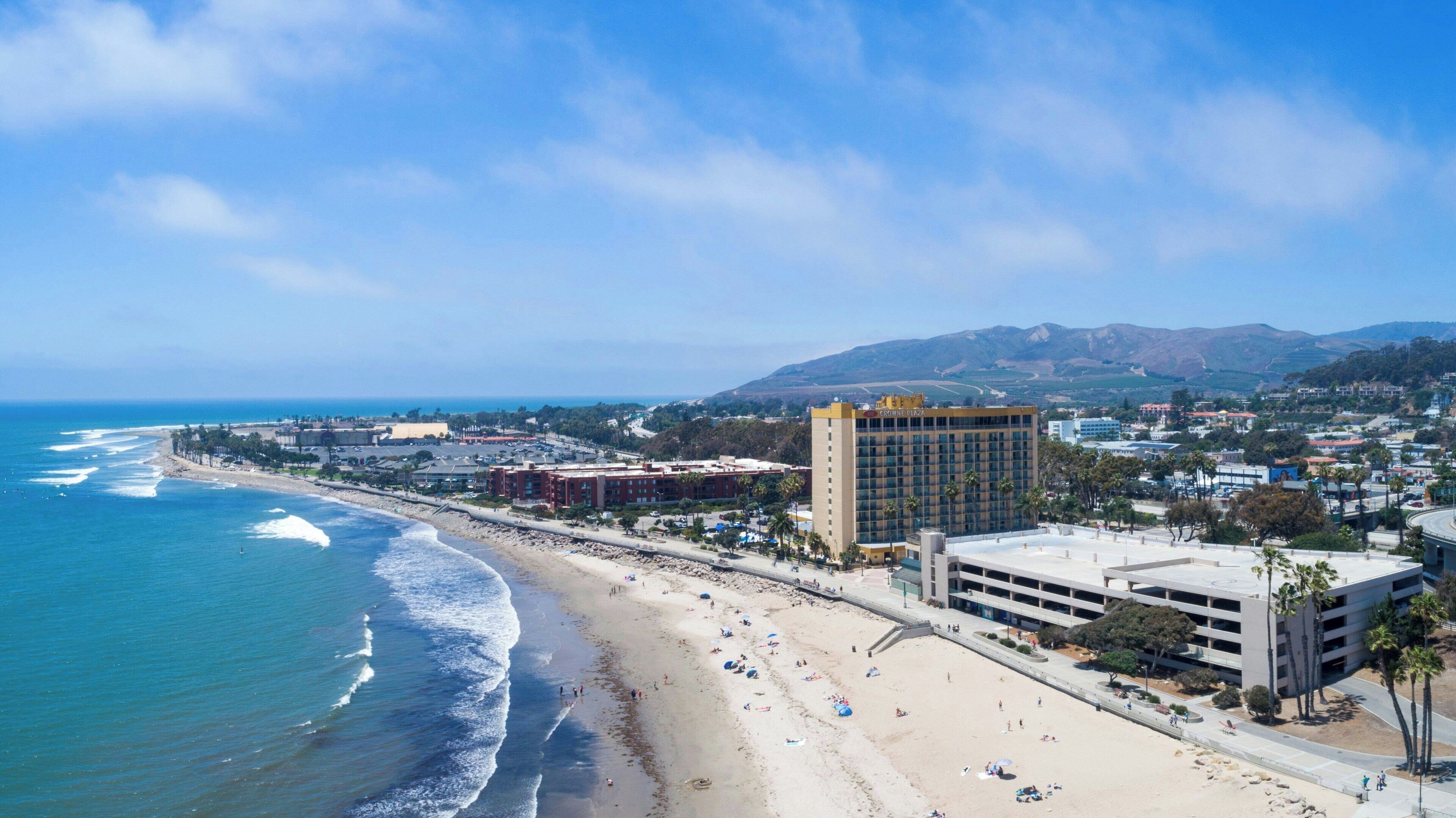 Un paisaje costero con playa, un hotel llamado Crowne Plaza y montañas al fondo.
